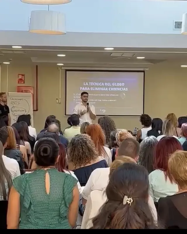 Alejandro con micrófono delante de una sala llena de asistentes, en otro evento