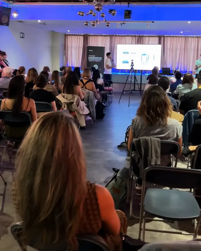 Sala de un evento llena de asistentes sentados, vista desde el fondo