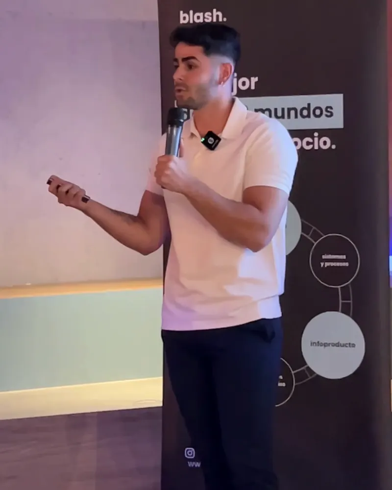 Alejandro Pinilla hablando con un micrófono en la mano durante una charla, delante de un cartel del evento